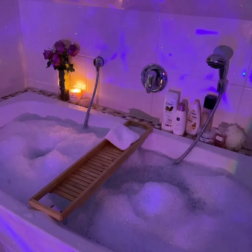 Violet lit bath with a wooden tray and fresh flowers